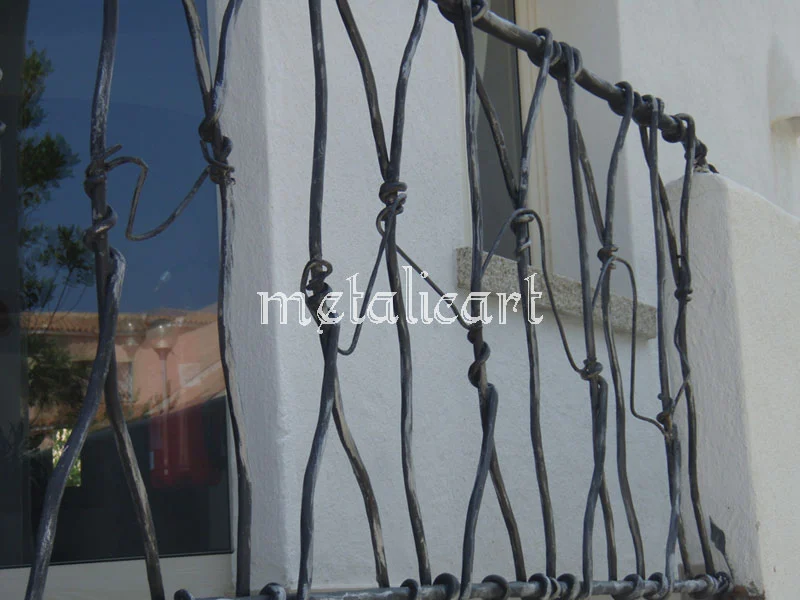 Detaliu de balustradă cu bare neregulate și noduri forjate, în lumină exterioară.