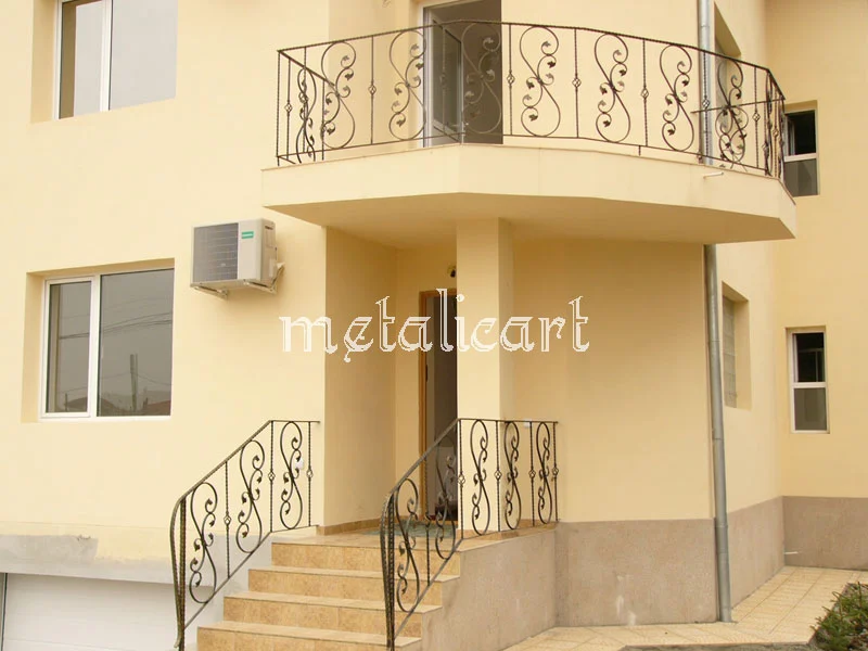 Balustrade de balcon și scară exterioară cu volute simetrice, pe fațada unei case.