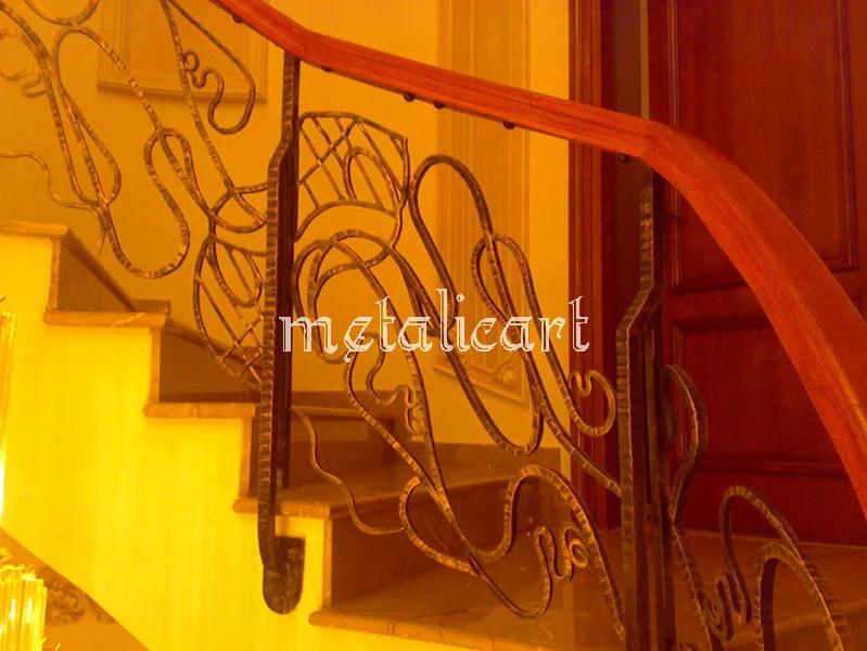 Detaliu de balustradă cu linii curbe libere și mână curentă de lemn, în lumină caldă.