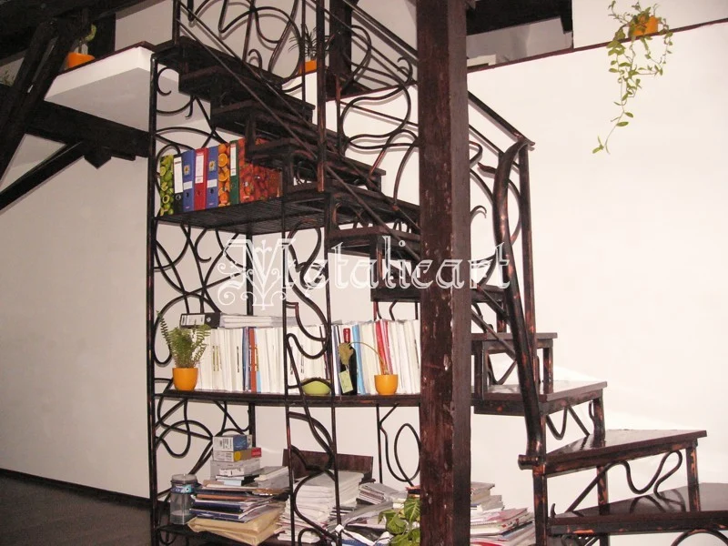 Scară interioară cu structură metalică forjată și vrejuri decorative, integrată cu rafturi de bibliotecă.
