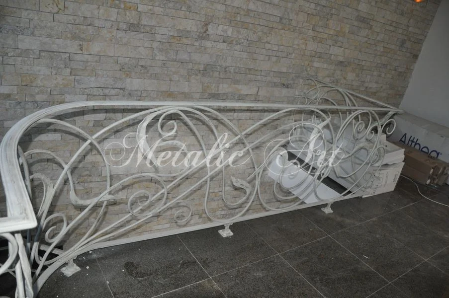 Balustradă albă cu desen curbat continuu, așezată de-a lungul unui perete de piatră.