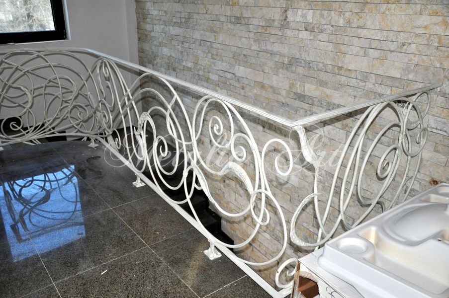 Balustradă albă de palier, cu bucle mari și linii unduite, pe fundal de piatră.