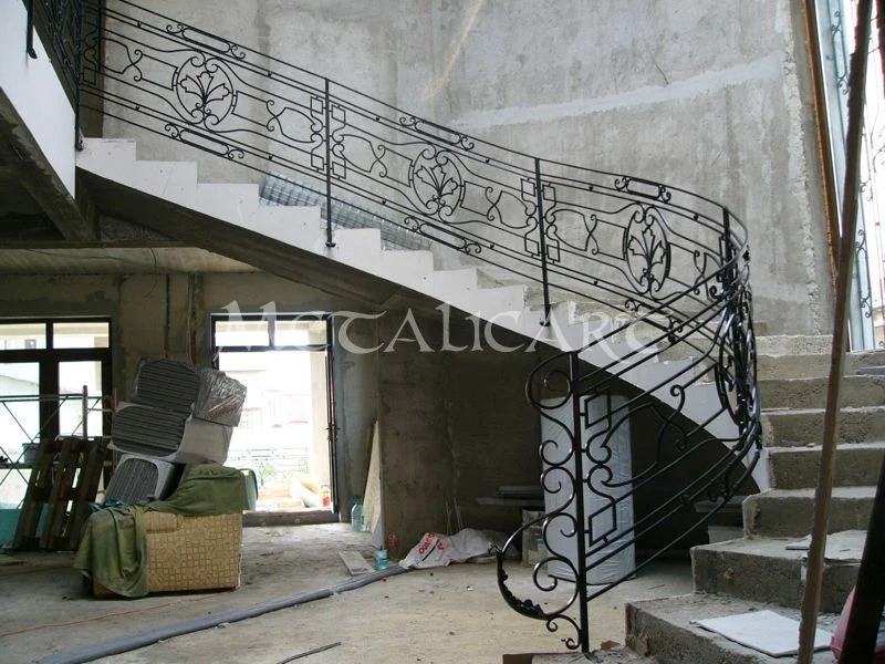 Balustradă de scară curbată, cu panouri repetate de volute, într-o clădire în construcție.