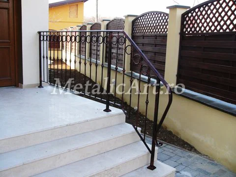 Balustradă exterioară de acces, cu inele repetate și mână curentă curbată, pe trepte de piatră.