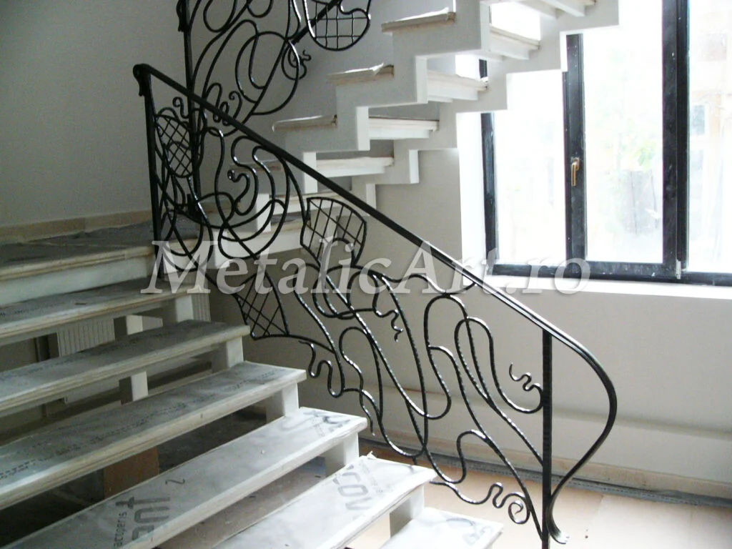 Balustradă de scară cu desen ondulat și panouri de plasă, lângă o fereastră mare.