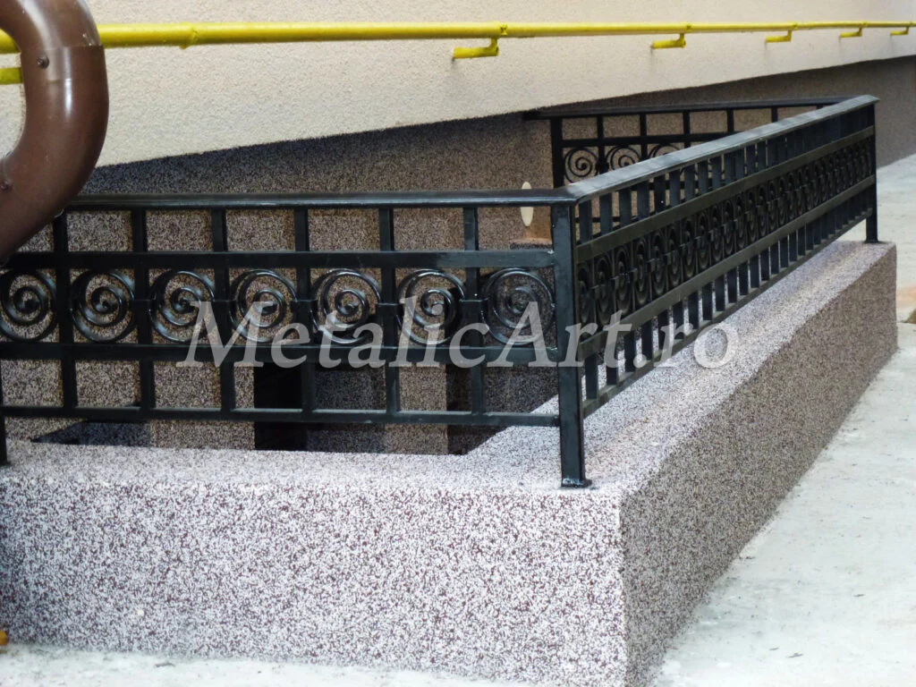 Balustradă exterioară cu rețea de pătrate și volute mici, pe soclu de beton.