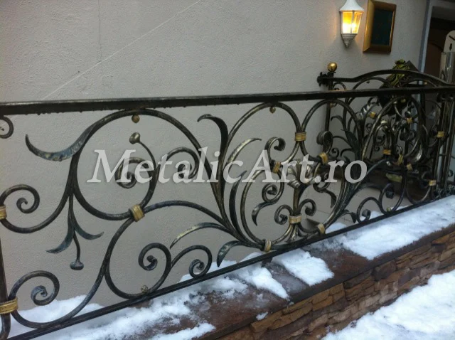 Balustradă exterioară cu volute și frunze, accente aurii, montată pe soclu de piatră.