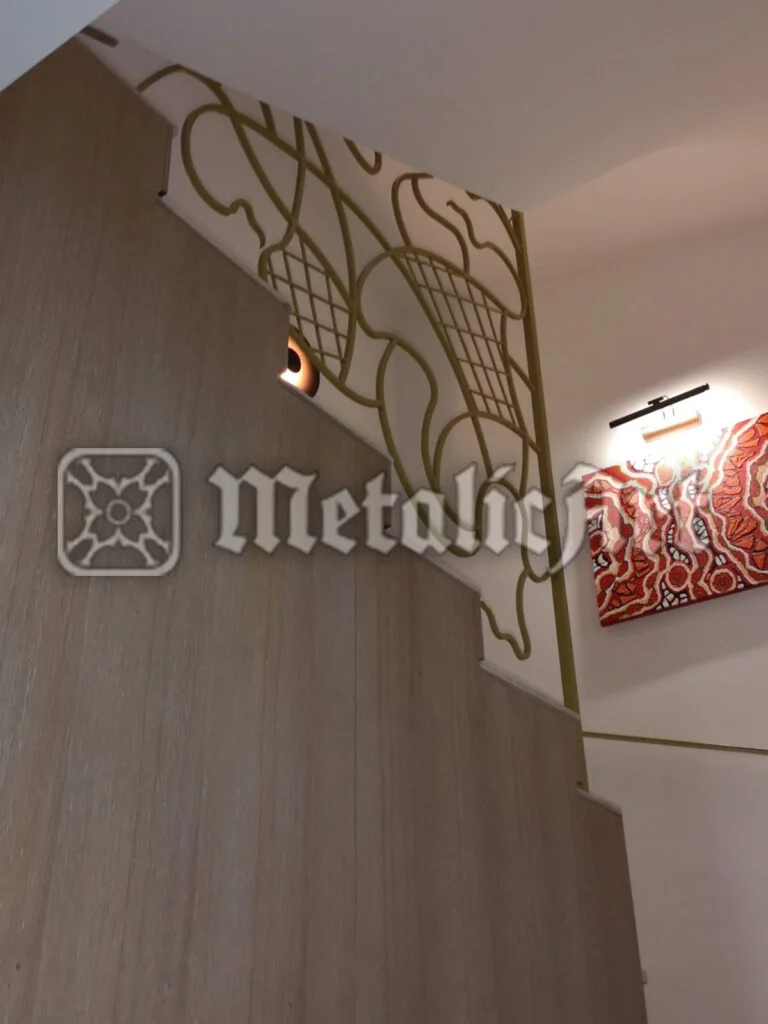 Balustradă cu desen vegetal traforat, finisaj auriu, montată de-a lungul rampei.