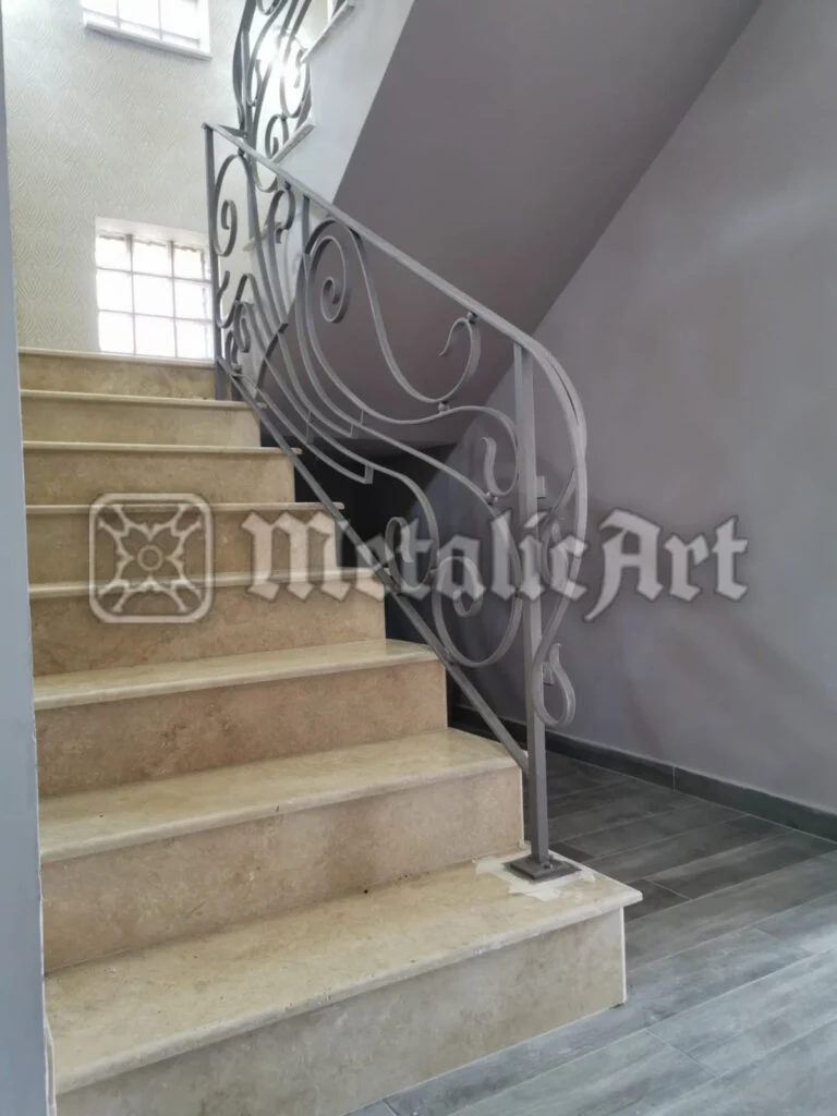 Balustradă cu desen curbat, asimetric, montată pe scară de piatră deschisă la culoare.