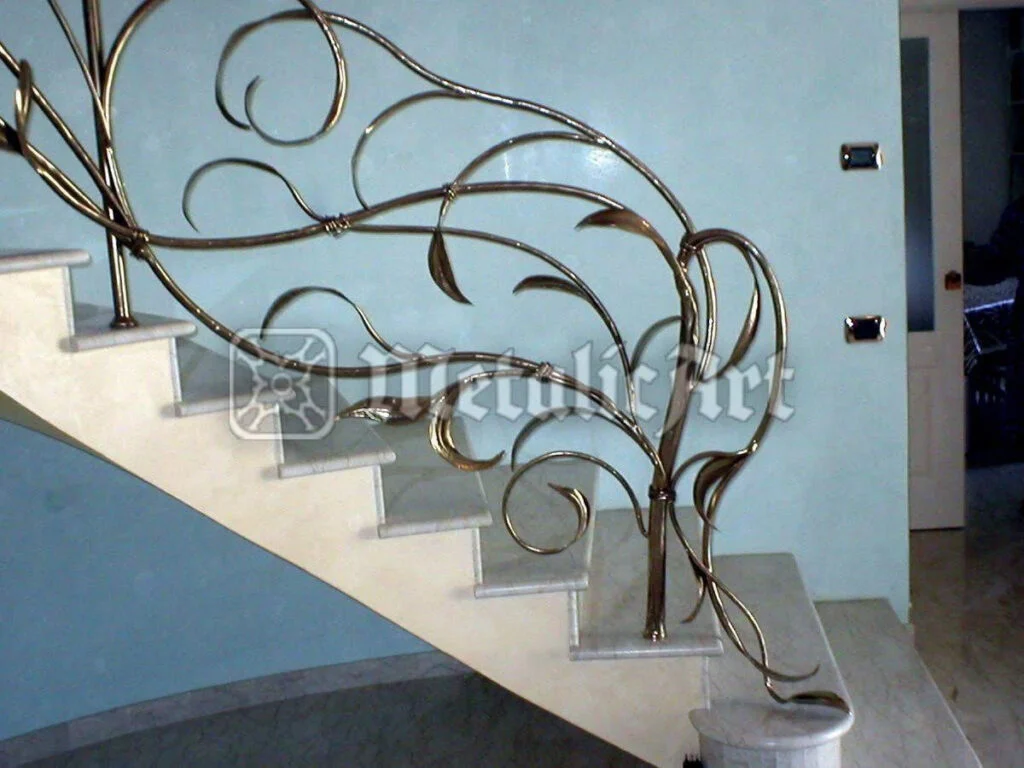 Balustradă cu ramuri și frunze forjate, finisaj auriu, montată pe scară curbată.