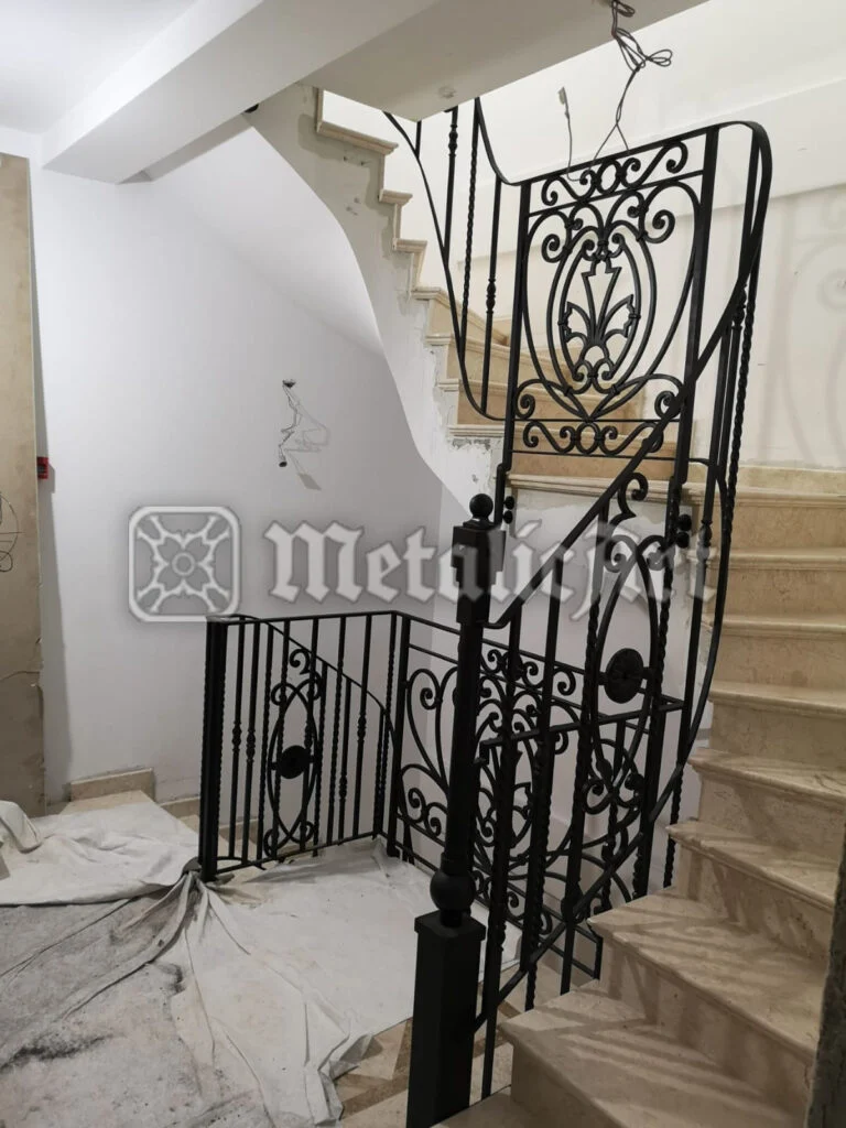 Balustradă de scară cu panouri ornamentale și stâlpi masivi, montată pe trepte de piatră.