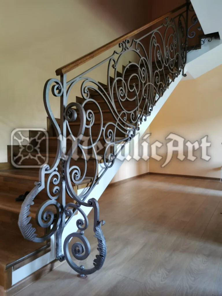 Balustradă interioară de scară, cu volute dese și frunze, sub mână curentă din lemn.