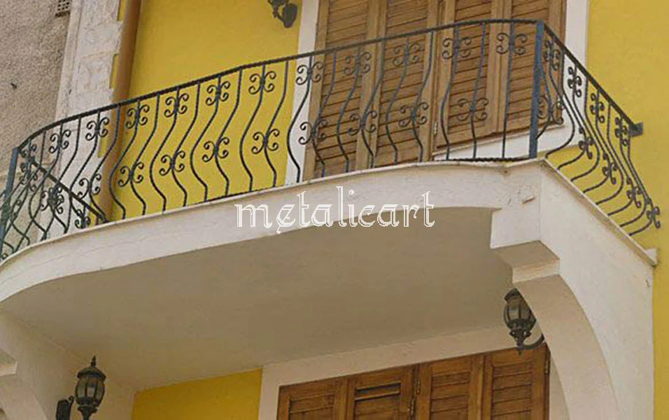 Balustradă curbată de balcon, cu bare ondulate și volute, pe fațadă galbenă.
