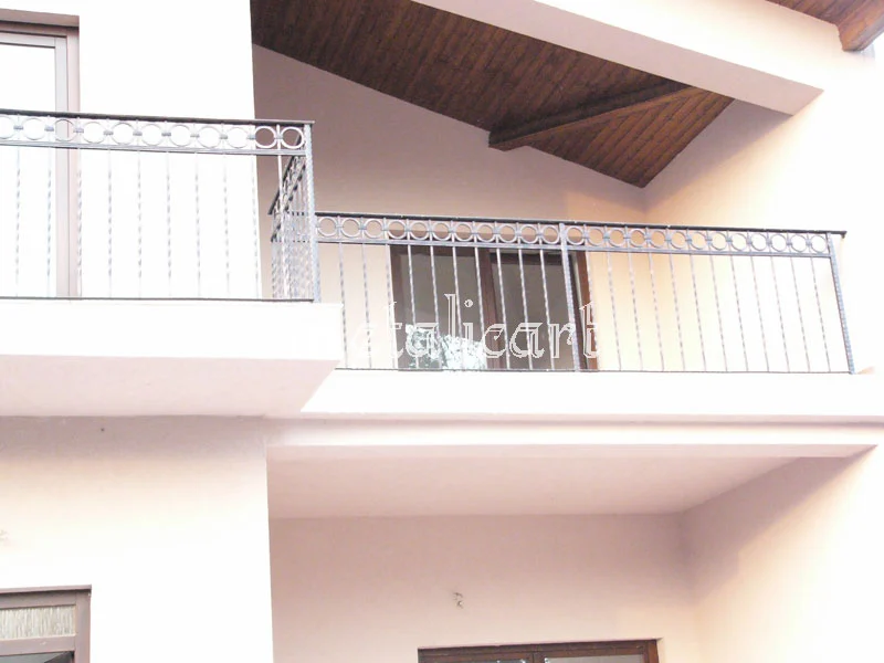 Balustrade de balcon cu bare verticale și friză de cercuri, la o casă cu streașină de lemn.