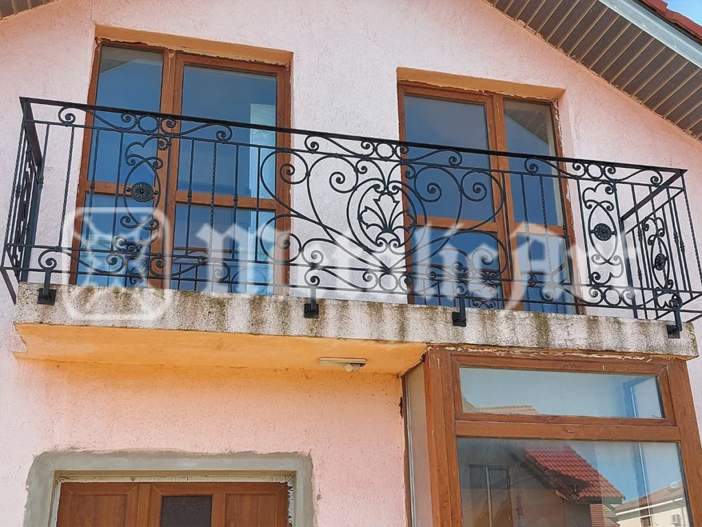Balustradă de balcon lungă, cu registru de volute și rozete, la o casă cu mansardă.