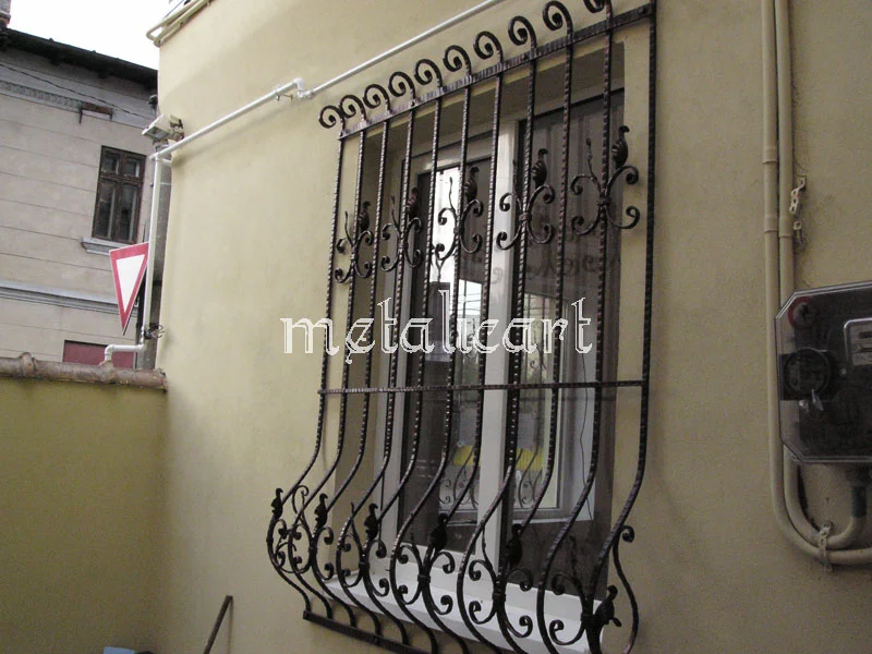 Grilaj bombat cu bare răsucite, volute la bază și vârfuri decorative în partea de sus.