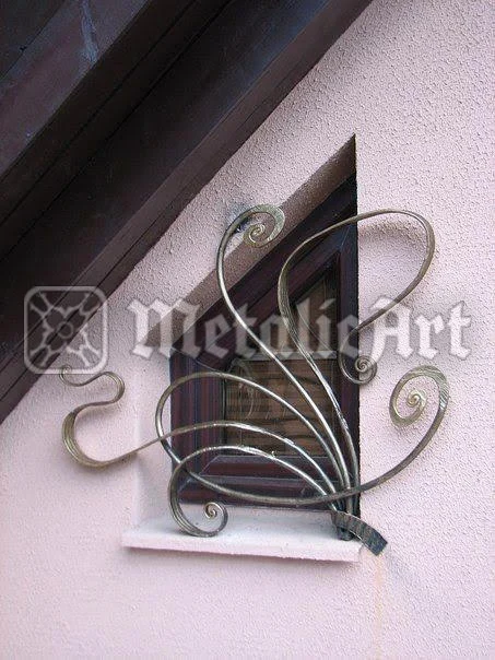 Grilaj decorativ cu volute mari asimetrice, montat pe o fereastră mică.