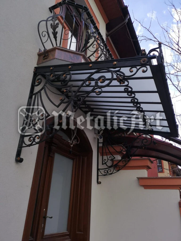 Copertină forjată cu ornament bogat de volute și vârfuri decorative, peste ușa de intrare.