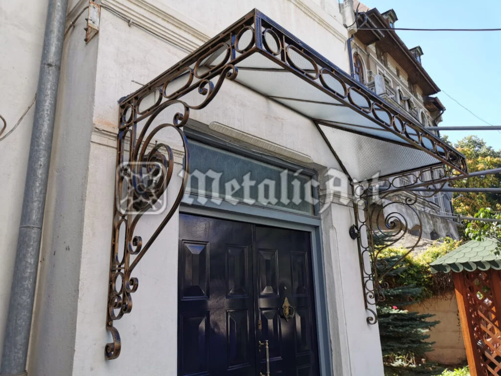 Copertină în două ape, cu ornament de volute și cercuri pe conturul frontal.