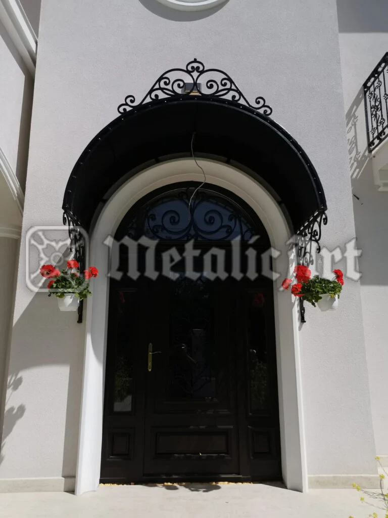 Copertină arcuită peste intrarea principală, cu ornament forjat pe conturul superior.