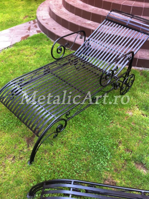 Șezlong de grădină din bare metalice curbate, cu volute laterale și roți decorative.