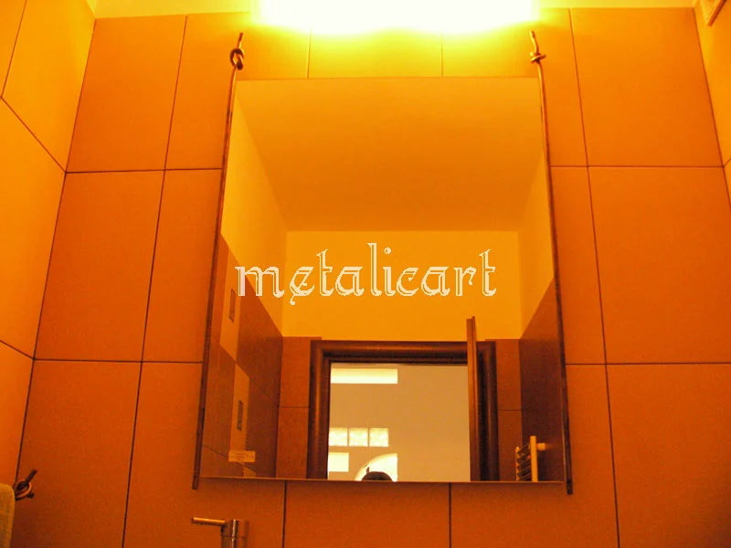 Oglindă cu ramă metalică subțire, montată pe un perete portocaliu.