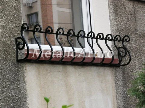 Suport de jardinieră forjat, cu volute, montat sub o fereastră.
