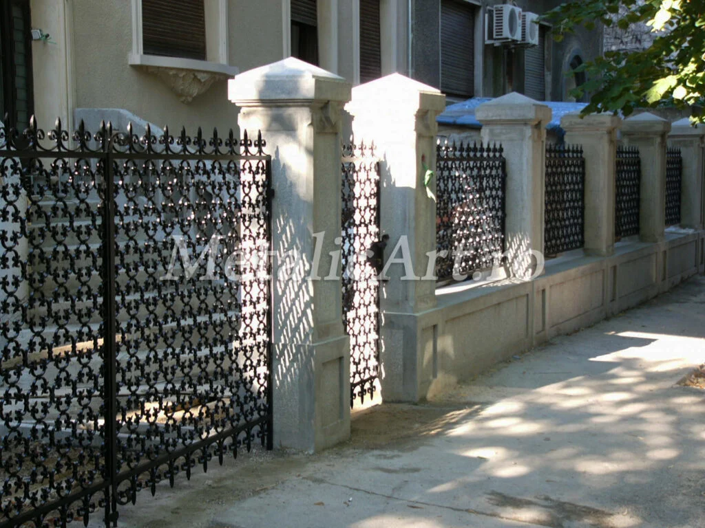 Gard cu panouri dense de crini și vârfuri decorative, între stâlpi de piatră.