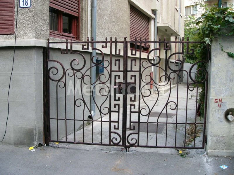 Poartă cu volute și motiv geometric în meandru, între ziduri tencuite.