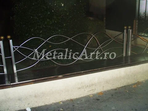 Panou de gard cu benzi metalice ondulate, întretăiate, în fața unei vitrine.