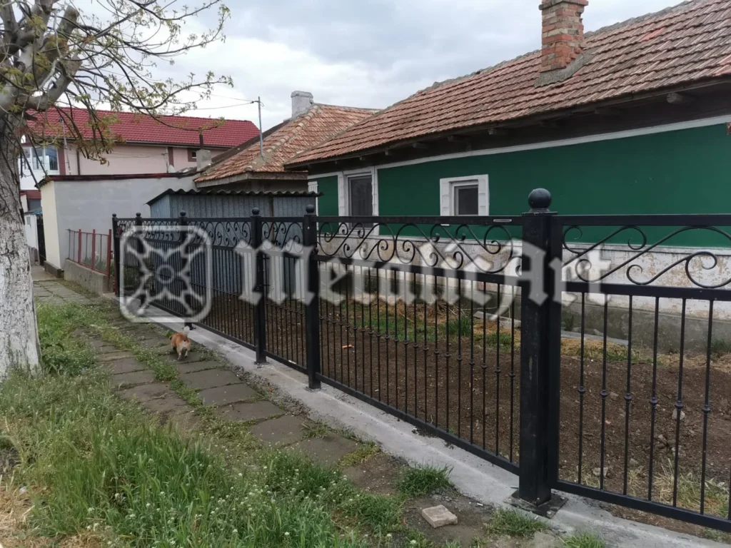 Gard cu bare verticale și volute superioare, de-a lungul unei alee.