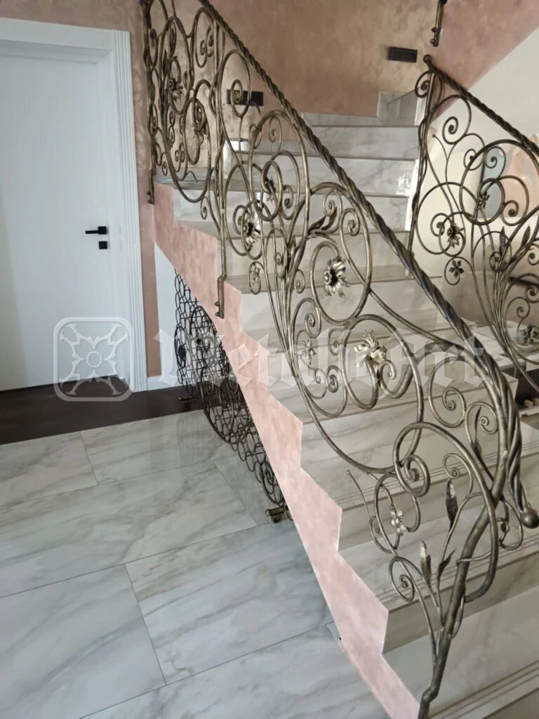 Rampa scării cu volute dese, văzută din hol, lângă ușa albă.