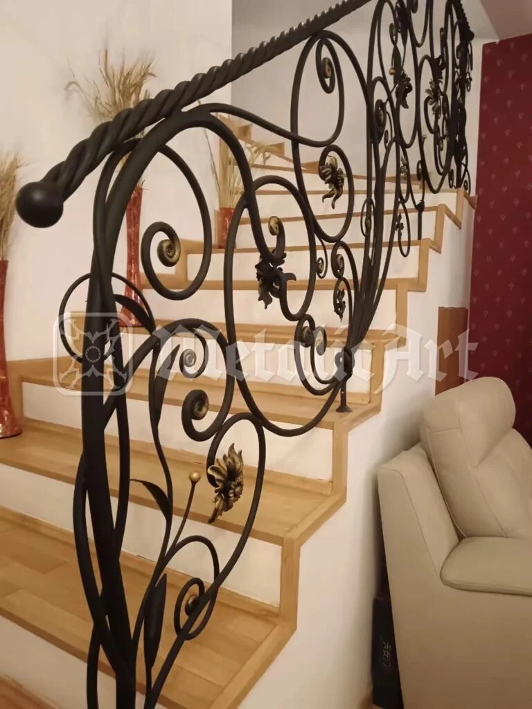 Rampa care urcă, cu frunze și flori forjate, lângă fotoliu.