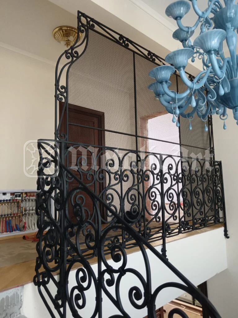 Balustrada din capul scării, sub candelabrul albastru.