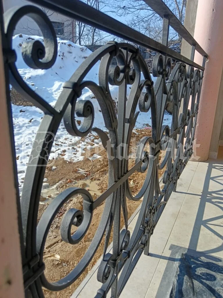 Balustrada terasei, între stâlpii roz, cu curtea în lucru dedesubt.
