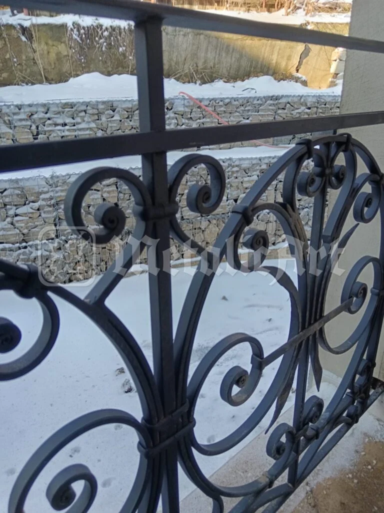 Panoul balustradei, cu volute, văzut pe fundalul zidului de piatră.