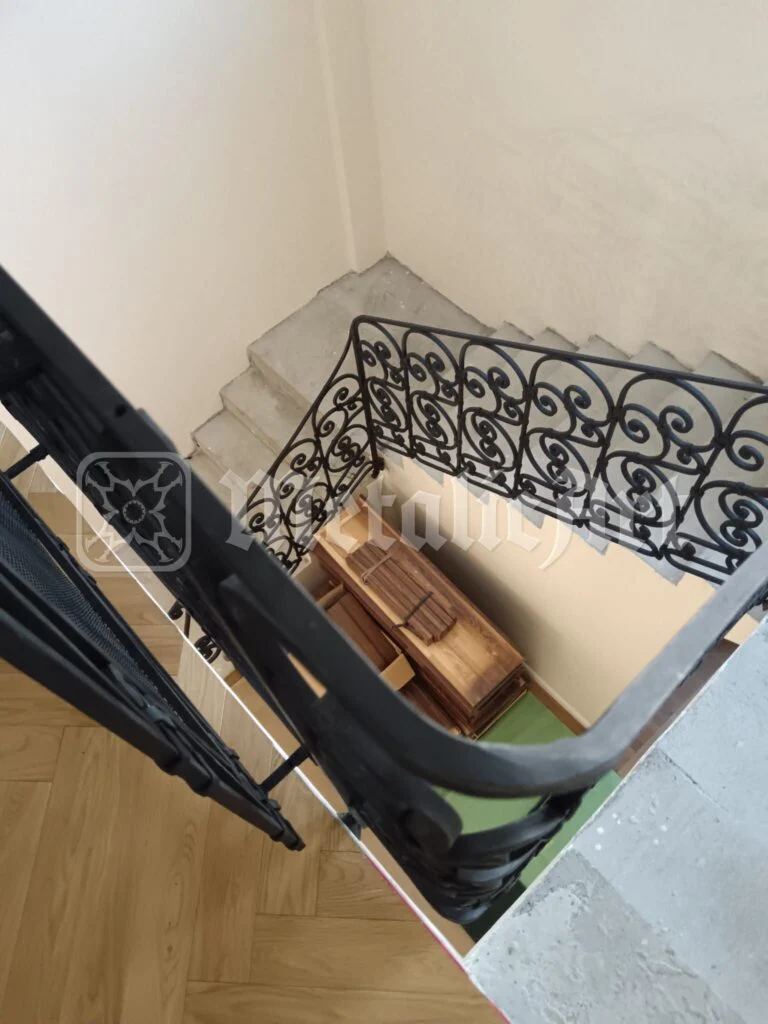 Scara văzută de sus, cu balustrada de volute coborând spre parchet.