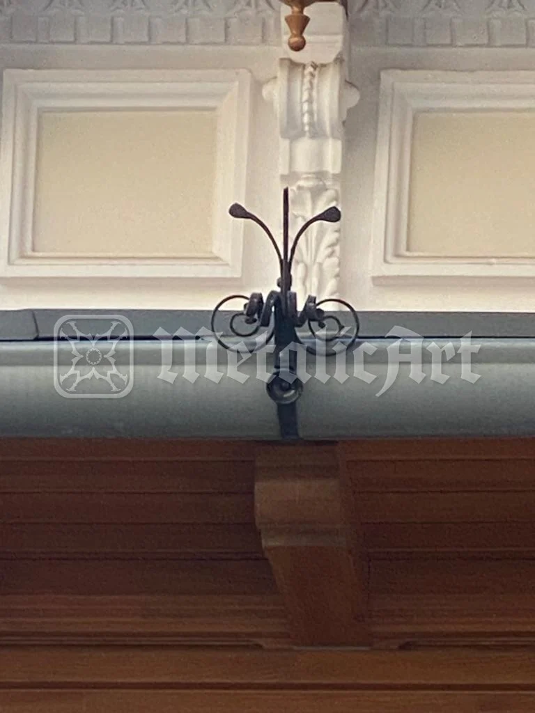 Detaliu: capătul forjat al unei bare, deasupra lambriului de lemn.