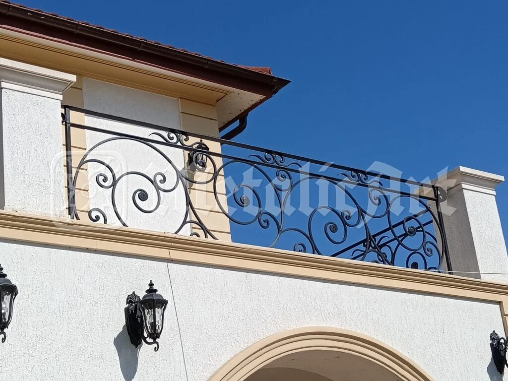 Balustrada terasei de la etaj, cu volutele ei, pe cerul senin.