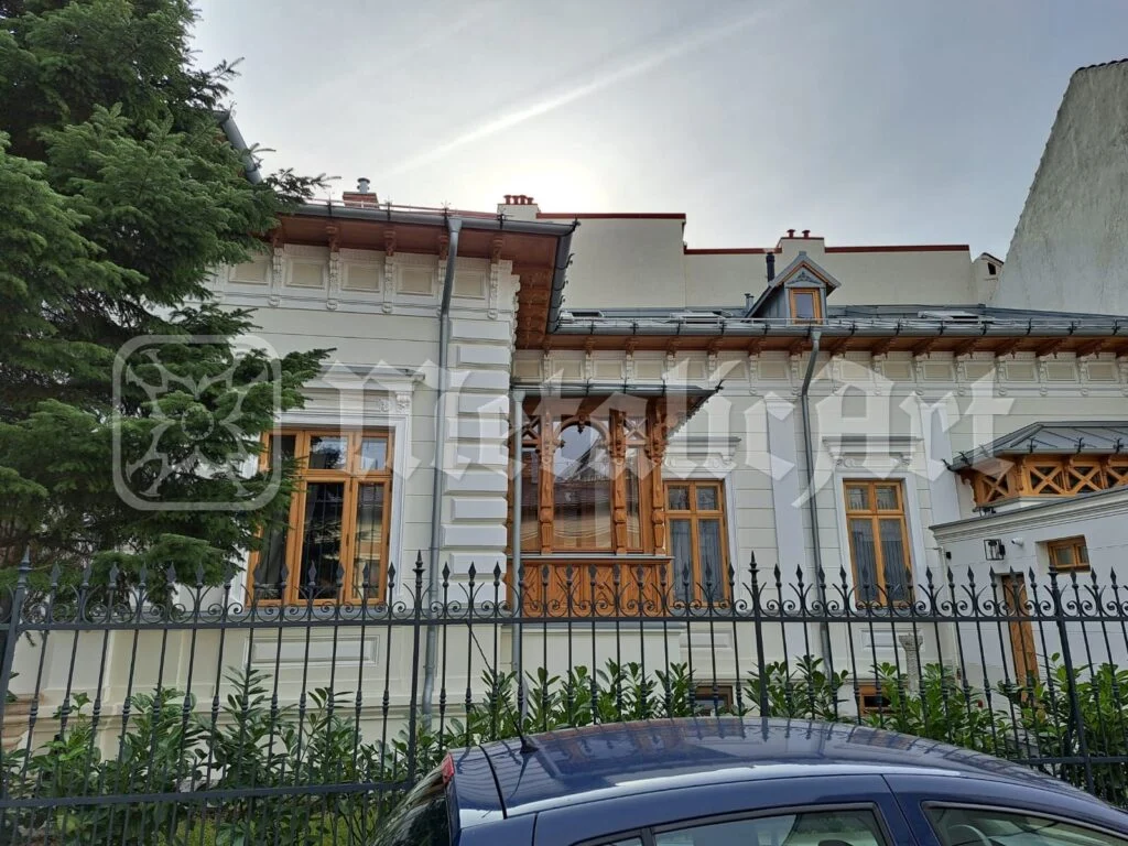 Fațada casei, văzută de peste gardul de fier.