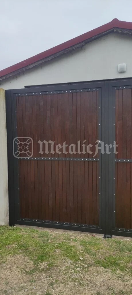 Canatul porții lângă zidul casei, cu nituri pe rama de metal.
