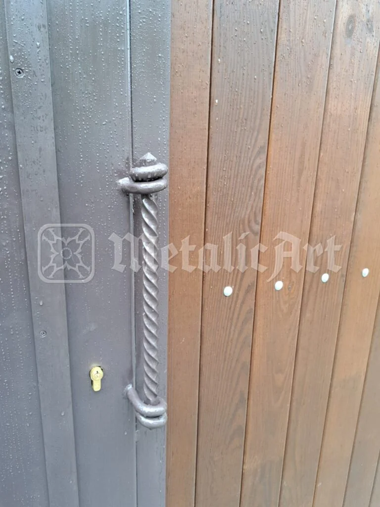 Mânerul răsucit al porții, pe canatul de lemn.