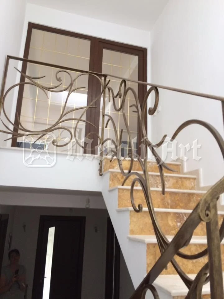 Balustrada cu linii curbe, văzută de jos, urcând pe treptele de travertin spre palier.