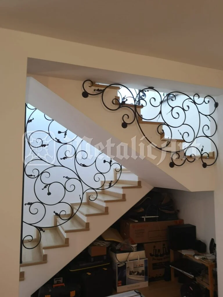 Balustradă de scară cu volute și mici flori forjate, montată sub o rampă albă.