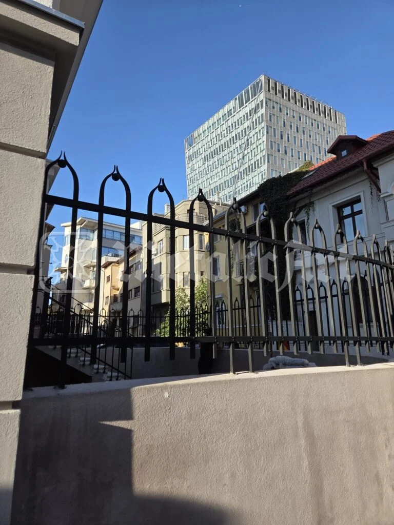 Gard din fier forjat spre stradă, cu orașul în fundal.