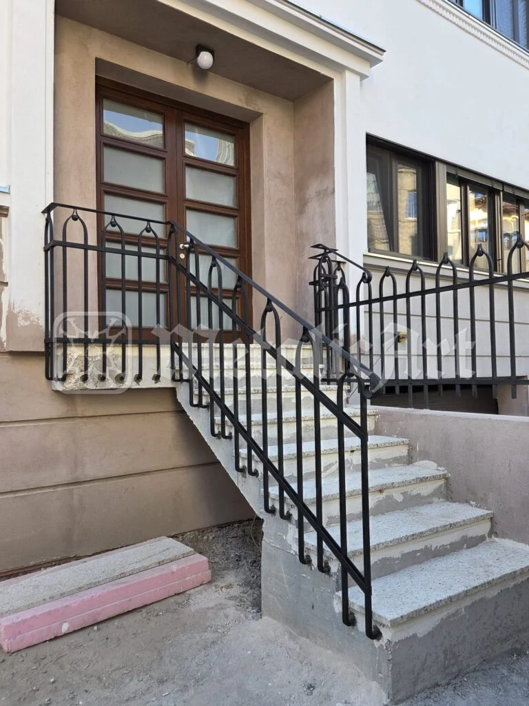 Trepte de intrare cu balustradă din fier forjat, în fața ușii de lemn.