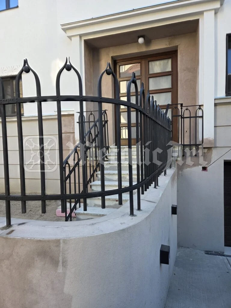 Balustradă din fier forjat cu arcade ogivale, curbată în fața intrării unei case noi.