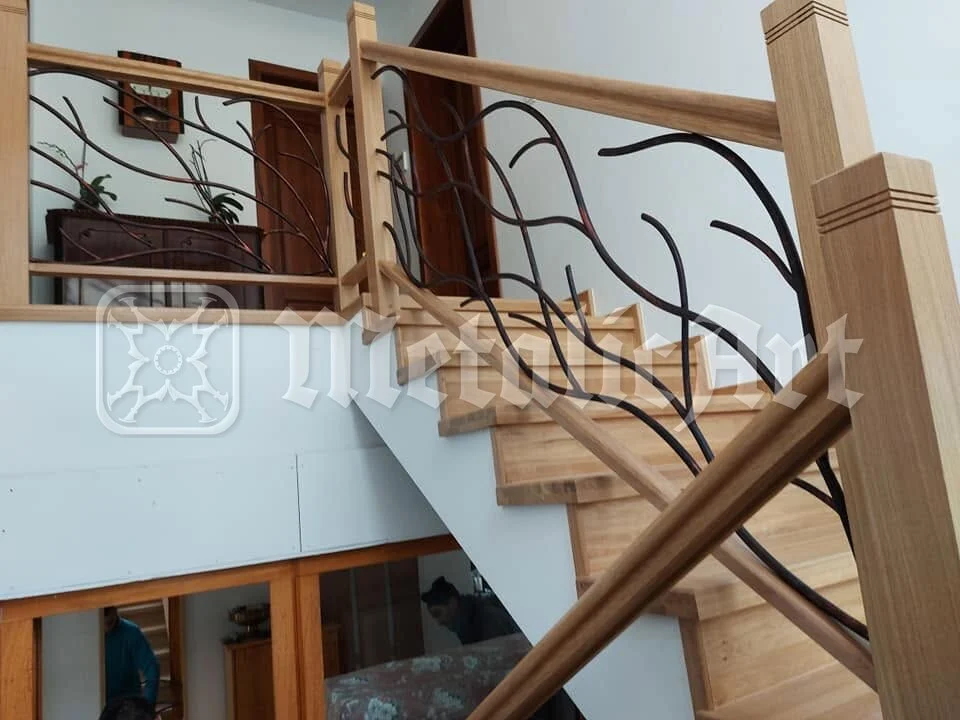 Balustrada cu desen de ramuri, prinsă între stâlpii de lemn.
