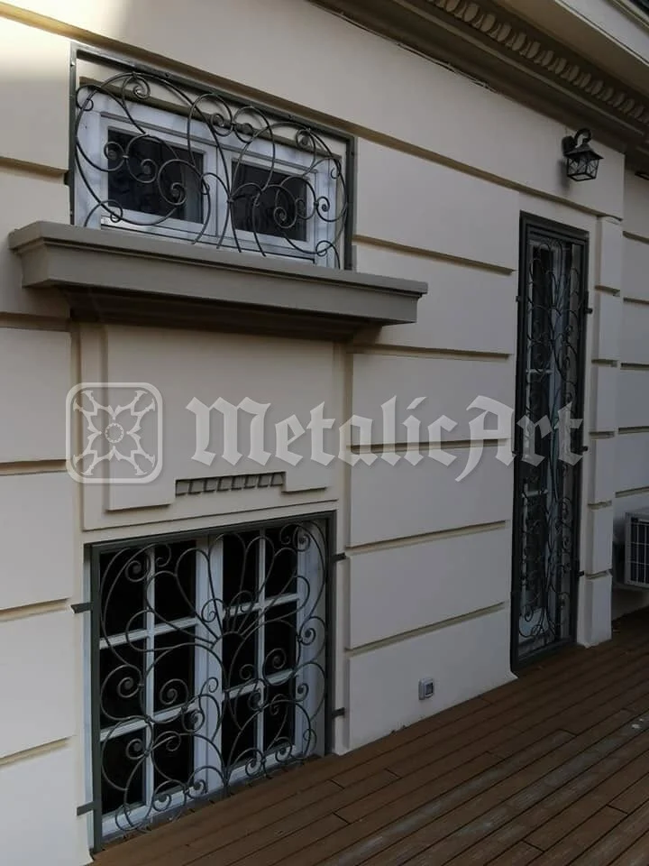 Două ferestre vecine, cu grilajele lor, sub cornișă.