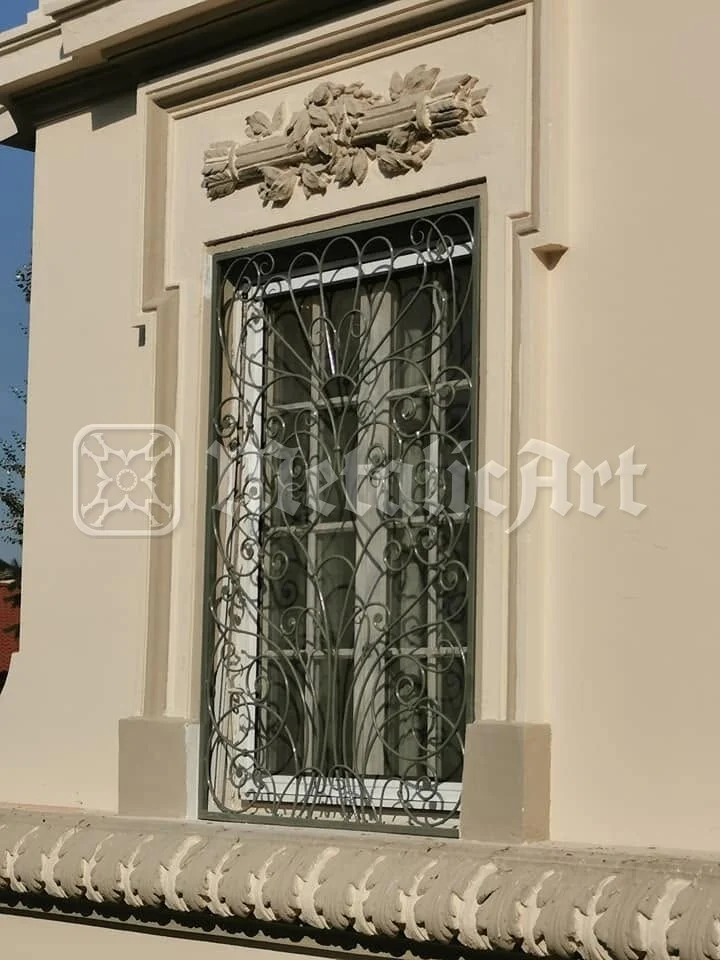 Fereastra cu ghirlandă de piatră deasupra, cu grilajul dedesubt.